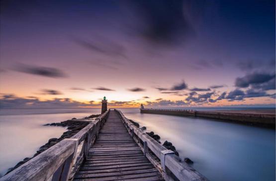 a pier with a lighthouse on the water at sunset at Villa Manita in Capbreton