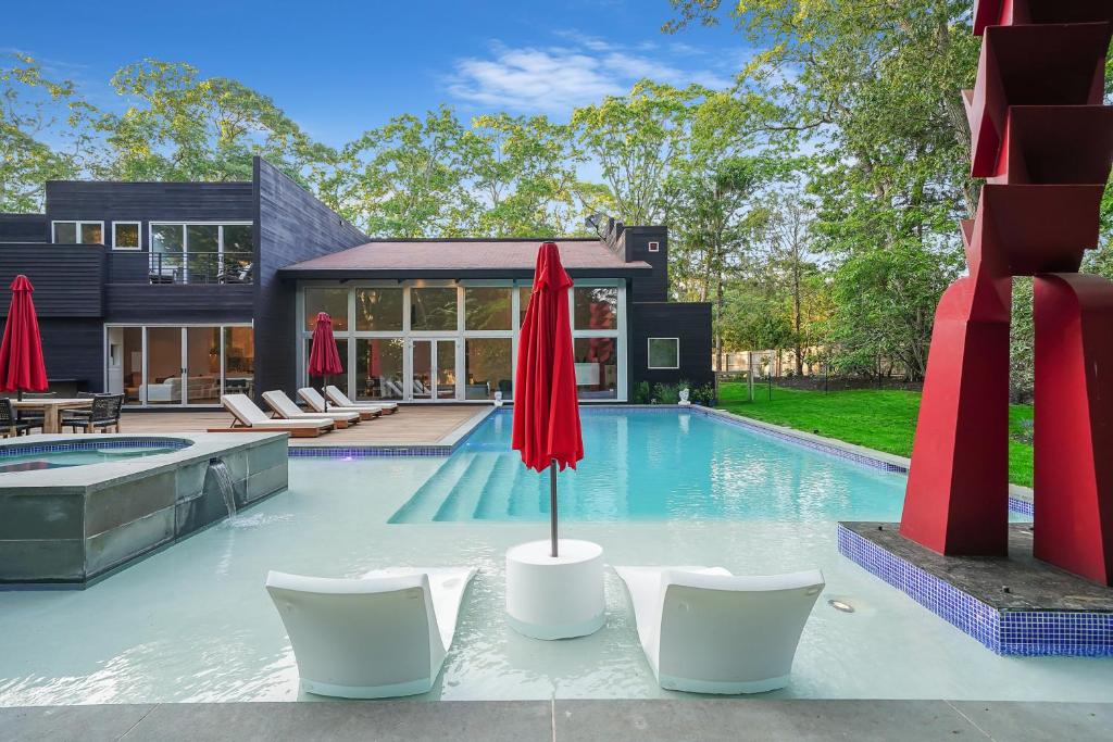 a pool with chairs and umbrellas in front of a house at Enjoy the Spa all year round in this EHV Estate in East Hampton