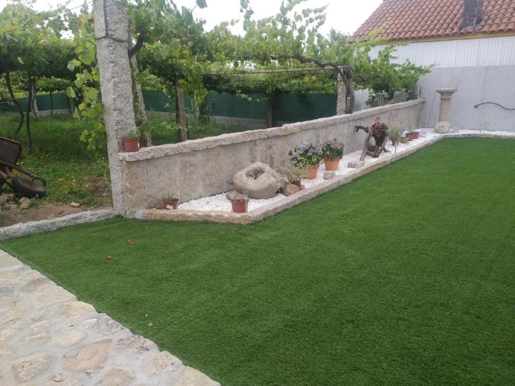 un jardín con césped verde y una pared de piedra en Casita con encanto entre viñedos, en Cambados