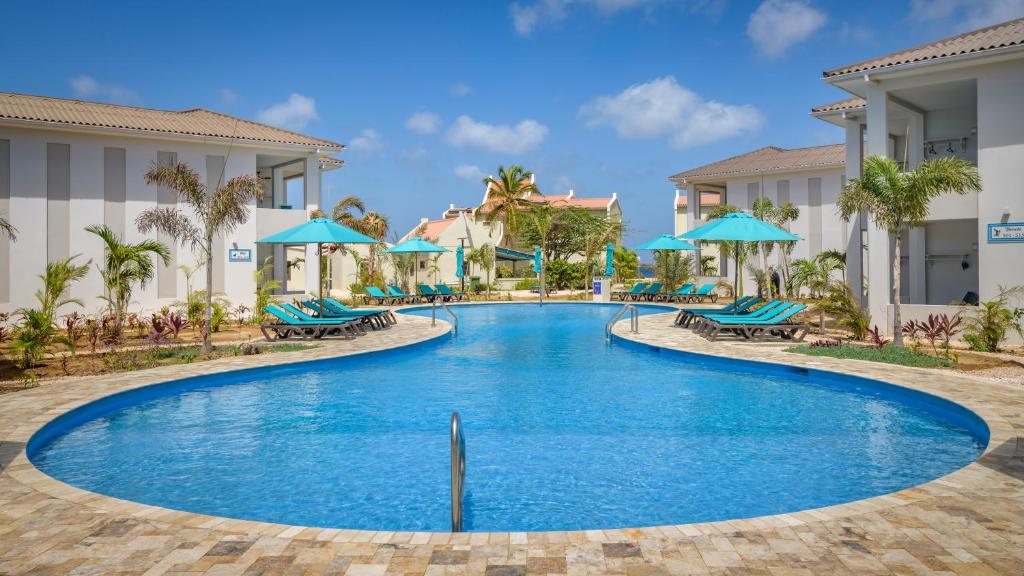 ein Pool in einem Resort mit blauen Sonnenschirmen in der Unterkunft Captain Don's Habitat in Kralendijk