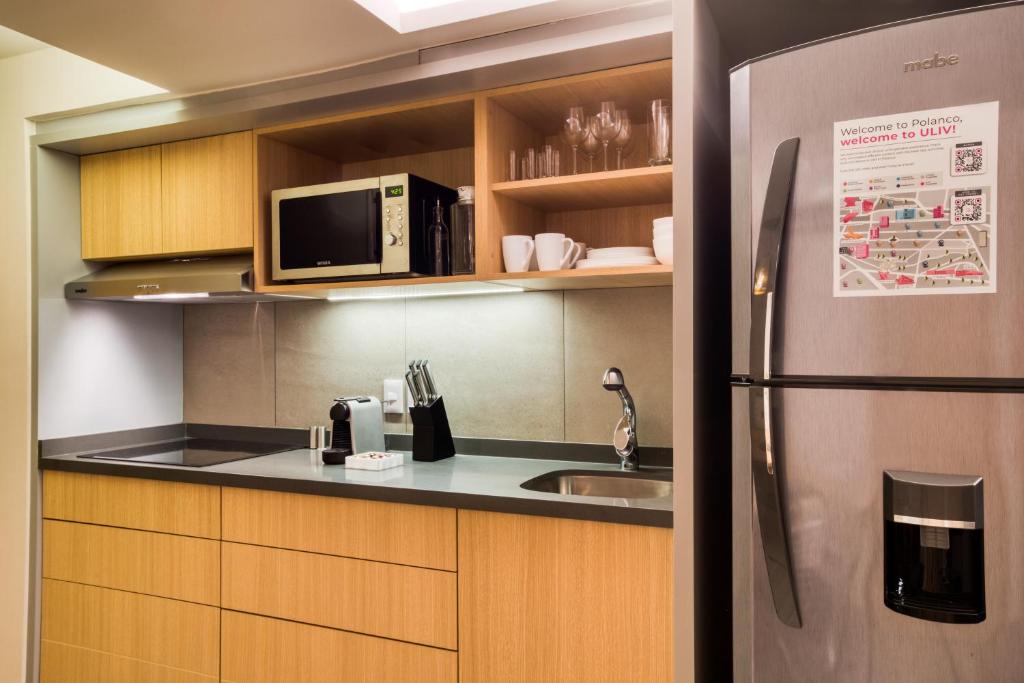 A compact kitchenette includes a sink, microwave, refrigerator, and open drinkware storage.