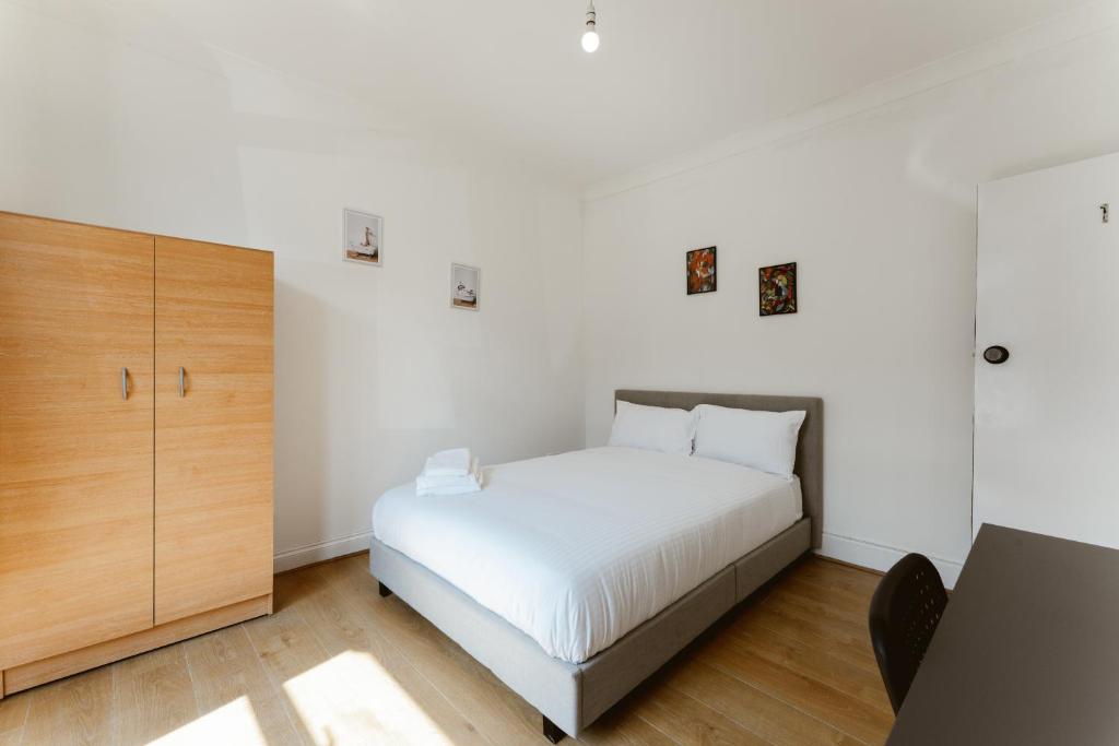 um quarto com uma cama branca e um armário de madeira em Plaistow Cosy Double Rooms - 8 em Londres