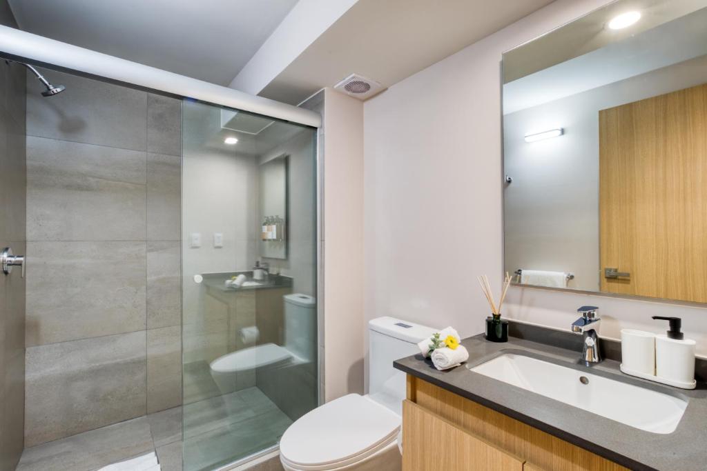 A bright bathroom combines a glass-enclosed shower, toilet, and wood-fronted vanity.