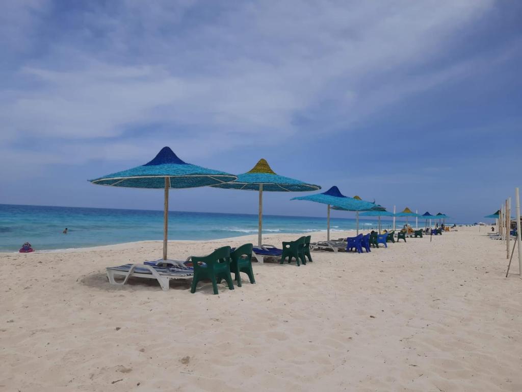 un grupo de sillas y sombrillas en una playa en مارسيليا بيتش ١ شاليه en Dawwār Abū al ‘Āşī