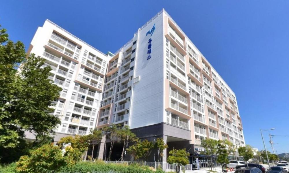 un edificio de apartamentos alto y blanco en un estacionamiento en Myeongga Ubleth Hotel en Yeosu