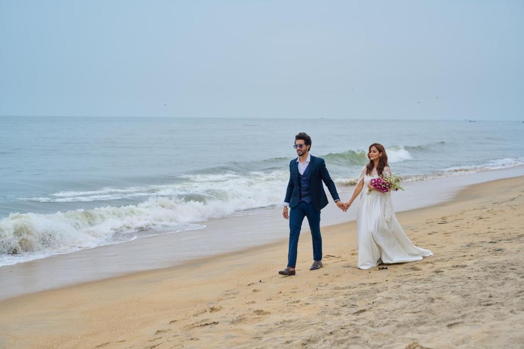 a bride and groom walking on the beach at Maliekal Heritance Cherai Beach Cochin in Cherai Beach