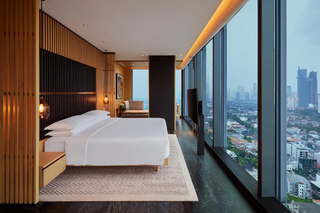 Park Hyatt Jakarta في جاكرتا: غرفة نوم بسرير ابيض ونوافذ كبيرة