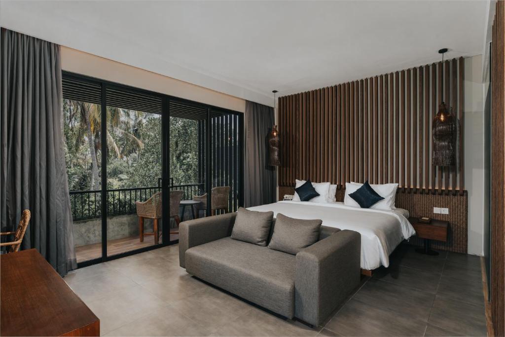 a bedroom with a bed and a chair and a window at The Ning Resort Ubud in Ubud