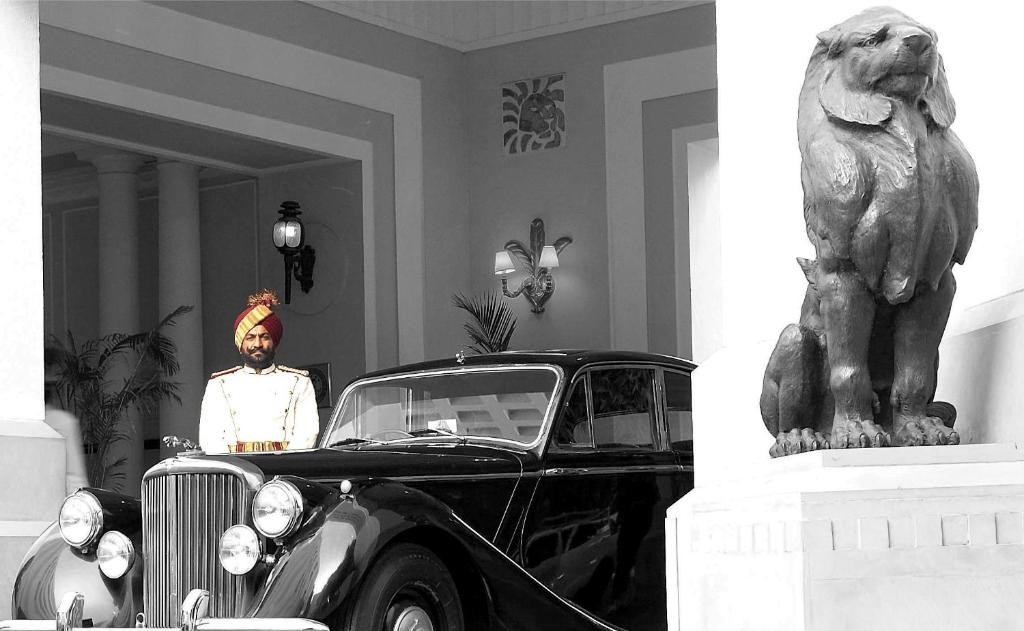 een man die naast een oude auto naast een standbeeld staat bij The Imperial, New Delhi in New Delhi