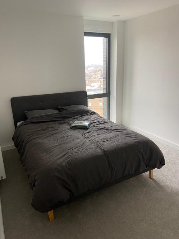 a bed with a black comforter in a room with a window at Spacious & Cozy One Bedroom Flat in Dagenham