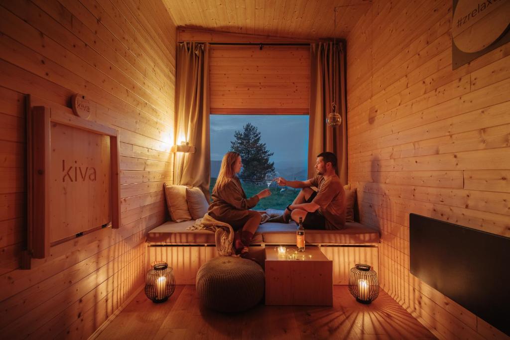 two people sitting on a couch in a room with a window at kiva cabin in Horné Hámre