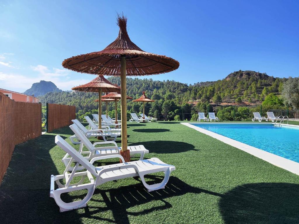 - un groupe de chaises longues et de parasols à côté de la piscine dans l'établissement Casa Rural E Puente del Segura, à Elche de la Sierra