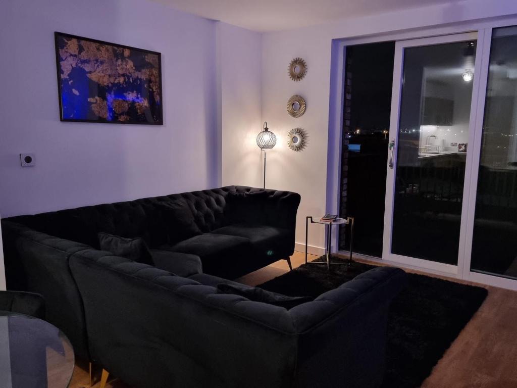 een woonkamer met een zwarte bank en een raam bij Lux One Bedroom Apartment in Barking