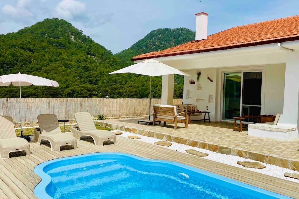 a house with a swimming pool with chairs and an umbrella at Villa Kuzyaka; 3 odalı, havuzlu, korunaklı in Fethiye