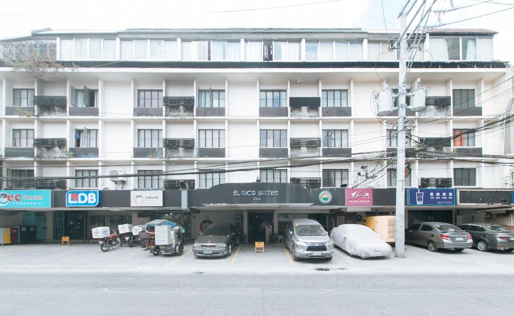 ein großes weißes Gebäude mit Autos auf einem Parkplatz in der Unterkunft El Rico Suite Makati by RedDoorz in Manila