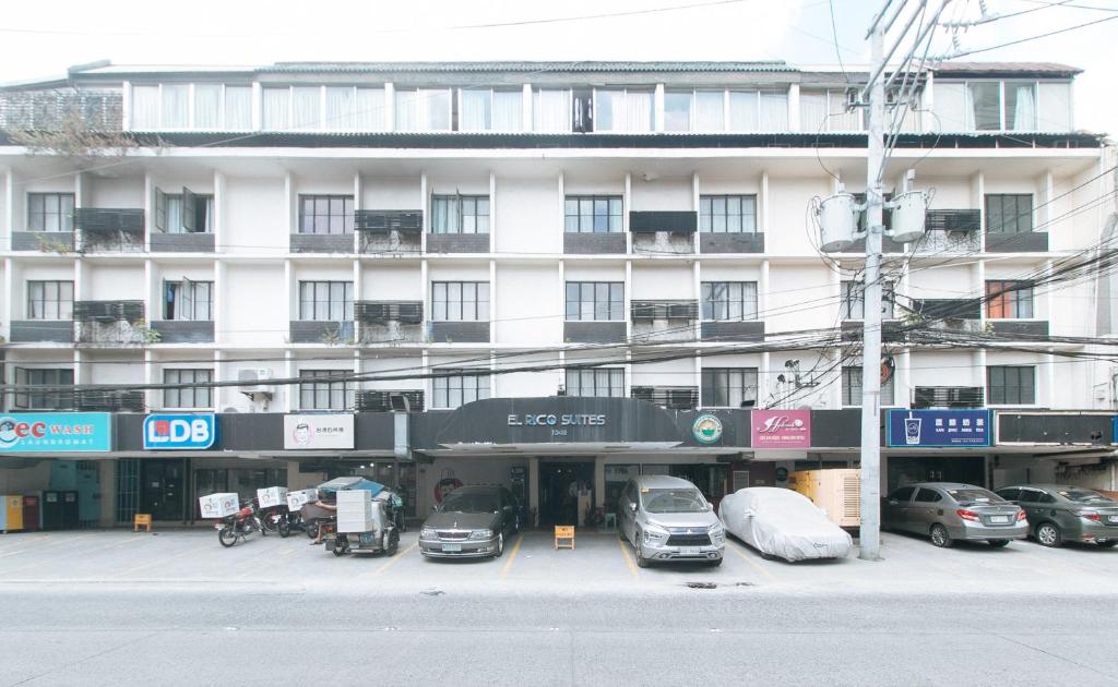 a large white building with cars parked in a parking lot at El Rico Suite Makati by RedDoorz in Manila