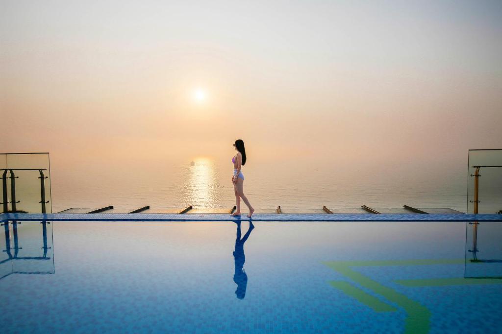 uma mulher a caminhar à beira de uma piscina em Maximilan Danang Beach Hotel em Da Nang