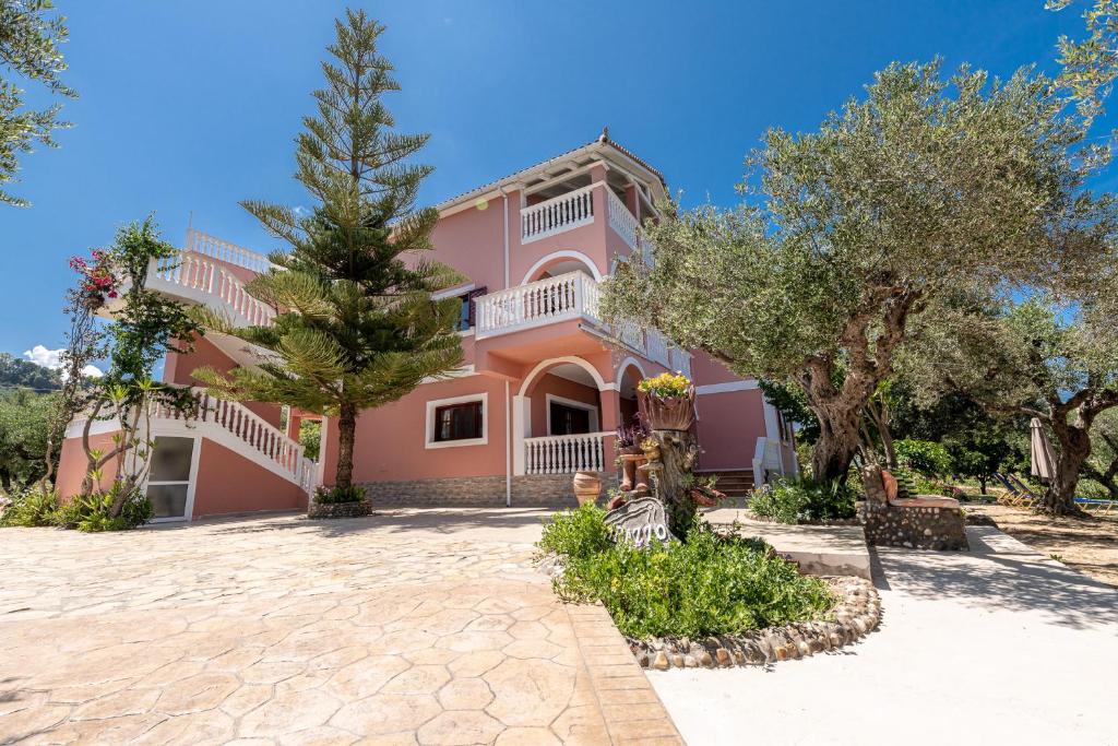 uma casa cor-de-rosa com árvores à frente. em Arazzo Apartments em Vasilikos