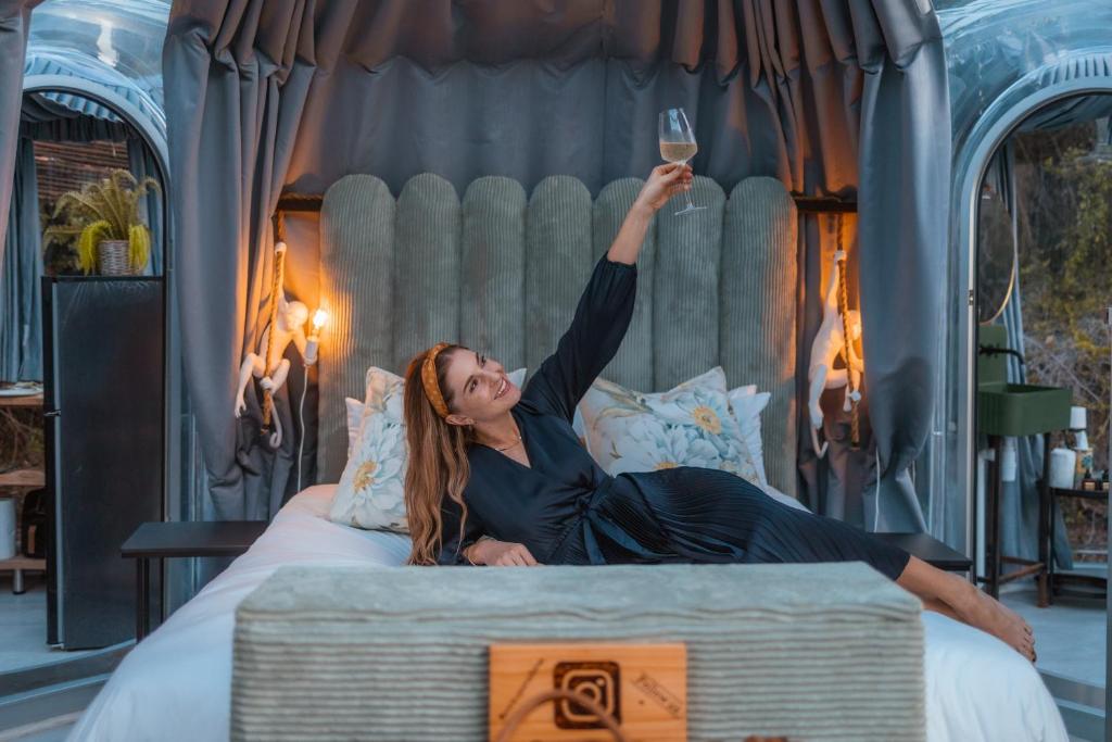 a woman laying on a bed holding a glass of wine at Stargazing Dome - Thunzi Bush Lodge in Beachview