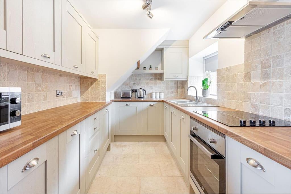 a kitchen with white cabinets and wooden counter tops at Woodrow End Cottage in Cawston