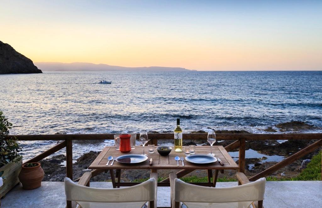 une table avec une bouteille de vin et des chaises donnant sur l'océan dans l'établissement Mochlos Waterside, à Mochlos