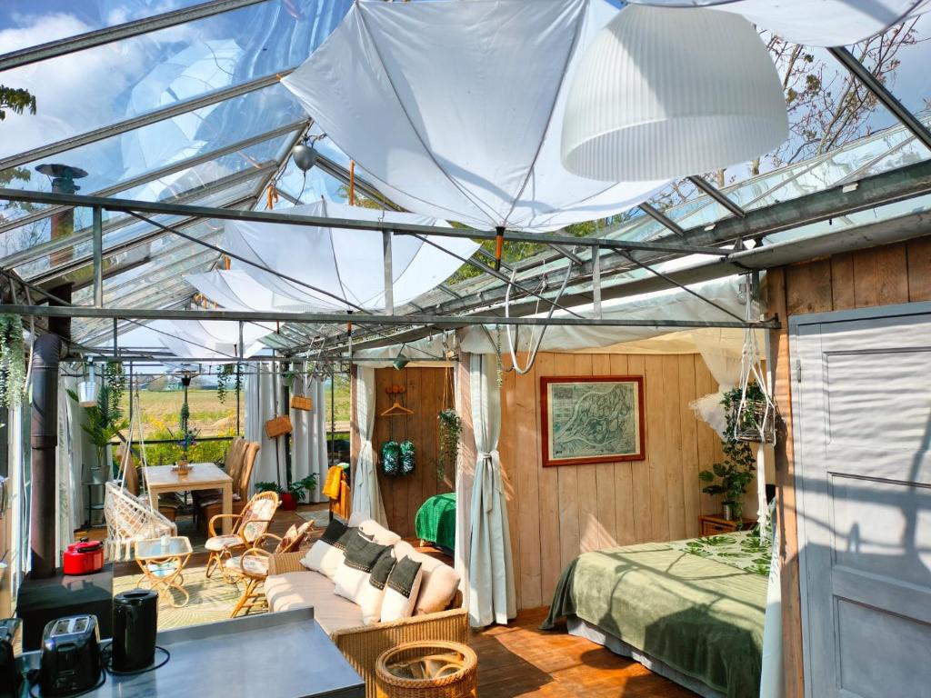 a glass house with a bed and a living room at Vrijstaande accommodatie Glamping de Kas InN in Hank