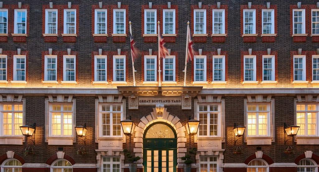 ロンドンにあるGreat Scotland Yard Hotel, part of Hyattの緑の扉と旗が二本の大きなレンガ造りの建物