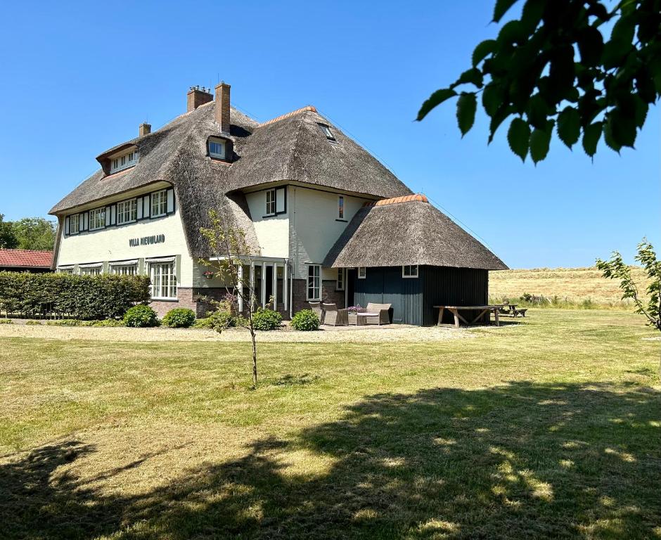 a large house with a thatched roof on a field at Villa Nieuwland B&B in Den Oever