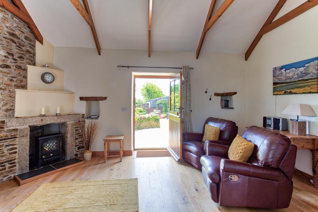 a living room with a leather couch and a fireplace at Rose Cottage, Tregolls Farm in Saint Wenn