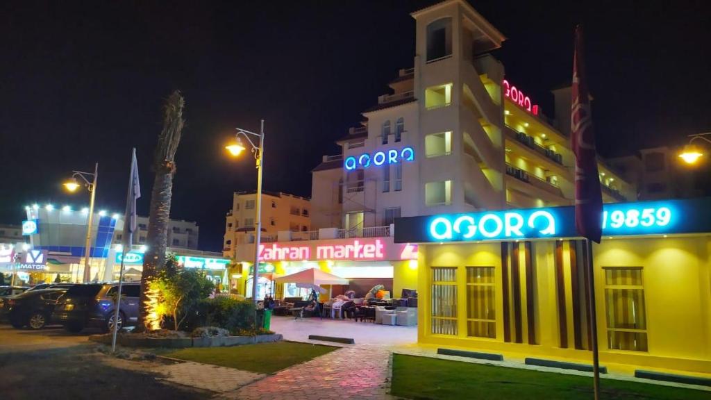 a building with neon signs on it at night at Agora in front of Marassi in Sīdī ‘Abd ar Raḩmān