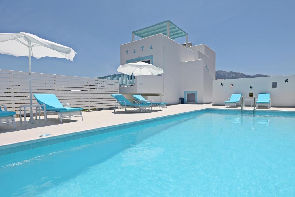 a swimming pool with chairs and umbrellas next to a building at Xenos Villa 7 with a Private pool near the sea in Tigaki