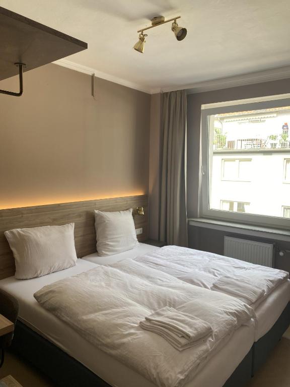 a bedroom with a bed with white sheets and a window at Hotel Petite Königsallee SELF CHECK-IN in Düsseldorf