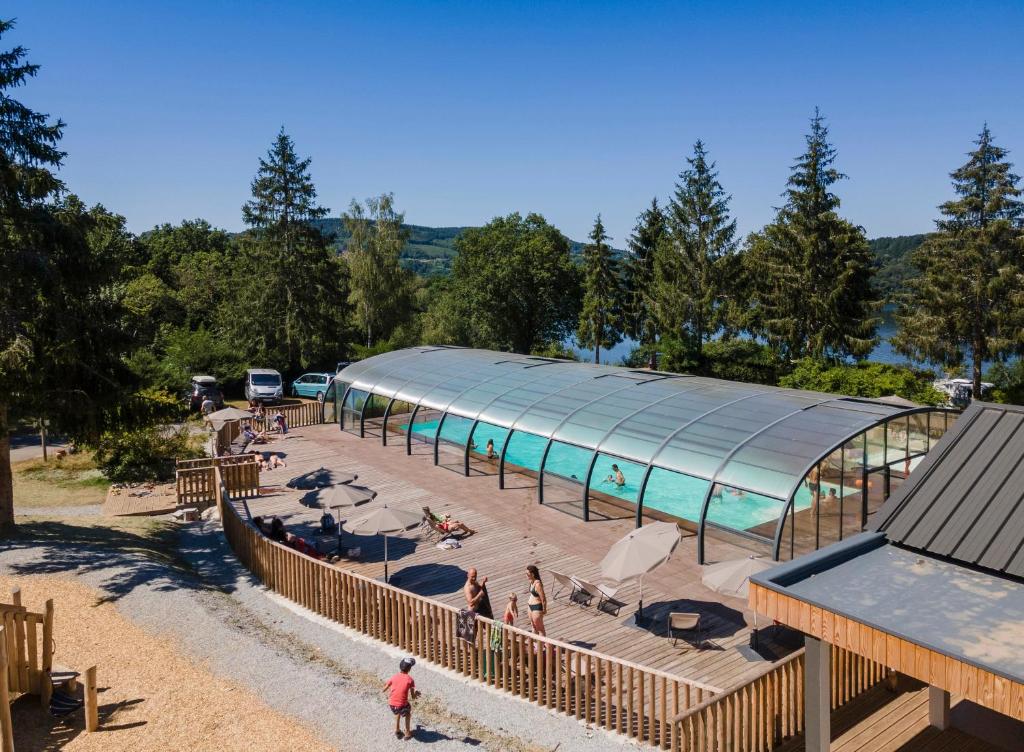 una piscina con una casa de cristal y gente a su alrededor en Huttopia Lac de la Siauve, en Lanobre
