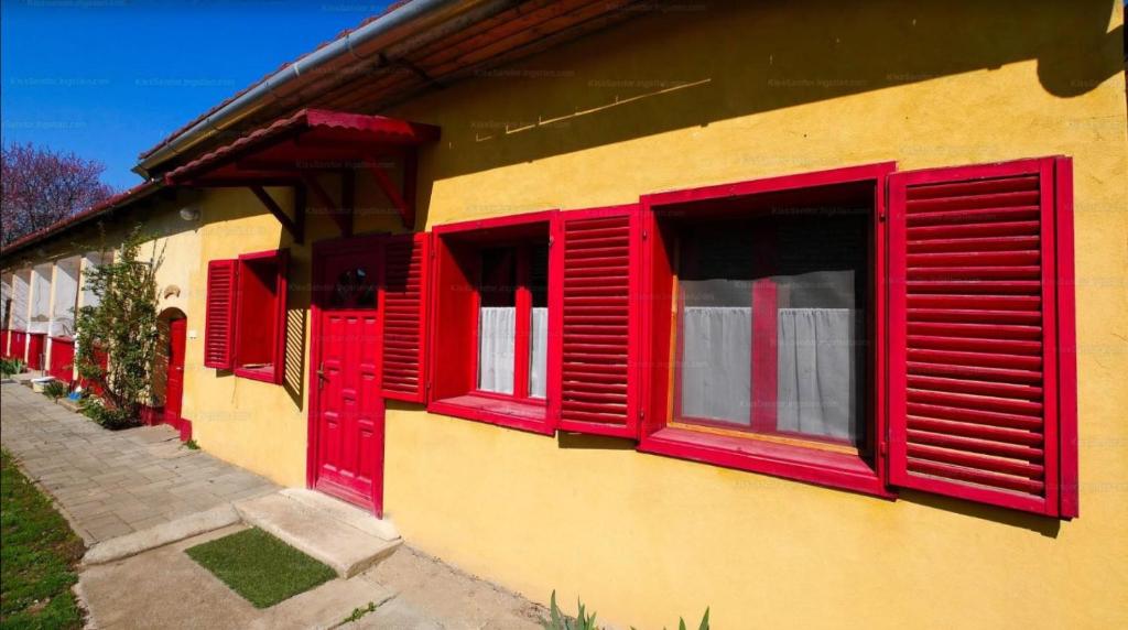 un groupe de fenêtres rouges sur un bâtiment jaune dans l'établissement Tornácos Vendégház - Kismarja, à Kismarja
