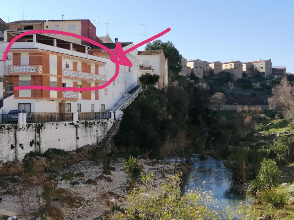 a building with a pink clock on it next to a river at Las Peñetas in Bolbaite