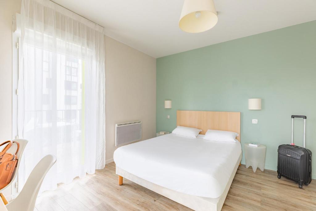 ein Schlafzimmer mit einem weißen Bett und einem Koffer in der Unterkunft Appart’City Confort Tours in Tours