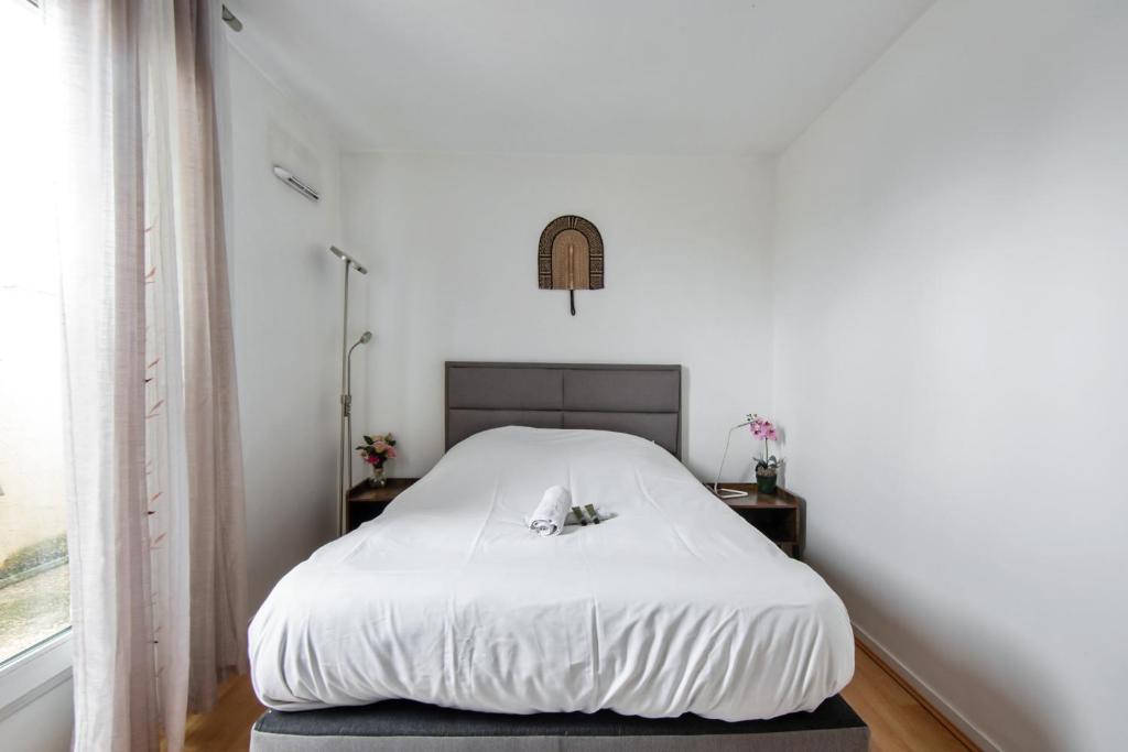 a white bed in a white bedroom with two tables at Charming 2br a 2 steps from the Stade de France - Welkeys in Saint-Denis