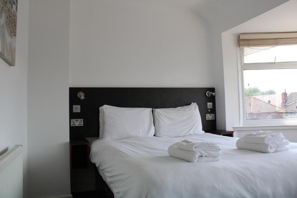 two towels on a white bed with a window at Cosy 3 bedroom house in quiet residential area in Manchester