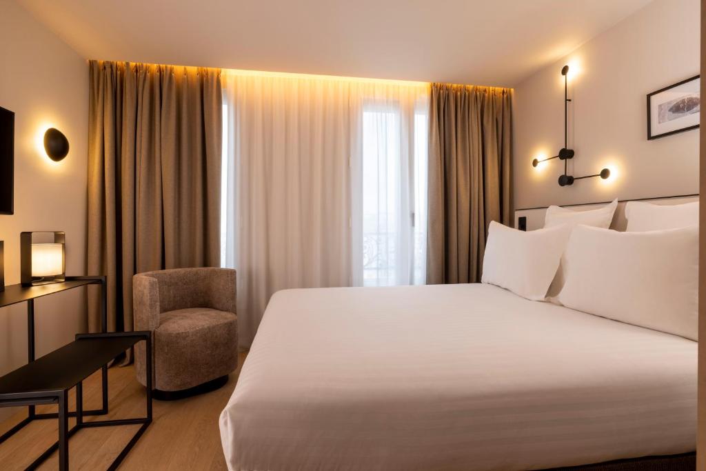 um quarto com uma grande cama branca e uma cadeira em Hôtel Esté em Paris