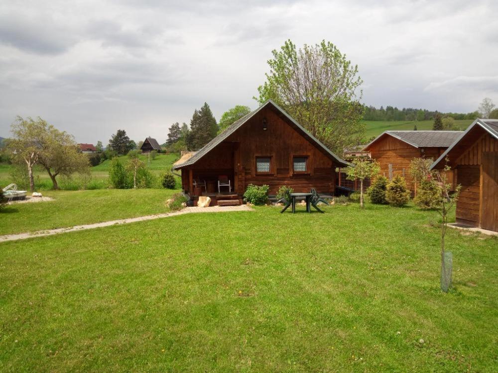 uma cabana de madeira com um relvado verde à sua frente em Chatky u Hromádky em Karlovice