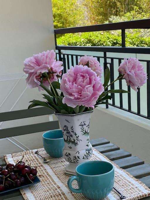 un vase avec des fleurs roses sur une table avec deux tasses dans l'établissement Joli studio calme et central, à Cannes
