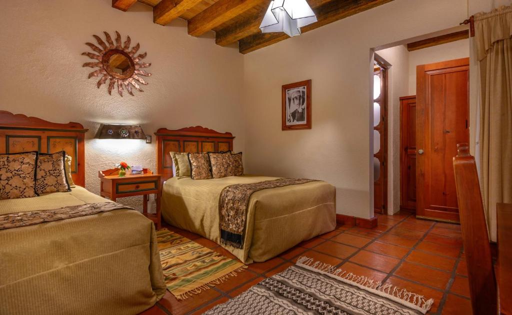 a bedroom with two beds and a table and a mirror at Hotel Pueblo Magico in Pátzcuaro