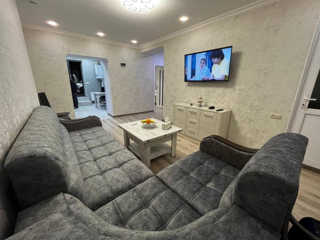 een woonkamer met een bank en een tv aan de muur bij Central Charm Guesthouse in Gjoemri