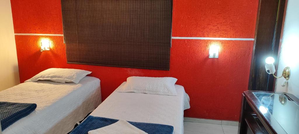 two beds in a room with a red wall at Sevili Garden Hotel in Arujá
