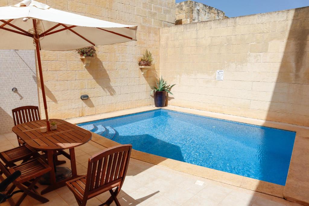 a swimming pool with a table and an umbrella at Rosehill B&B in Xagħra