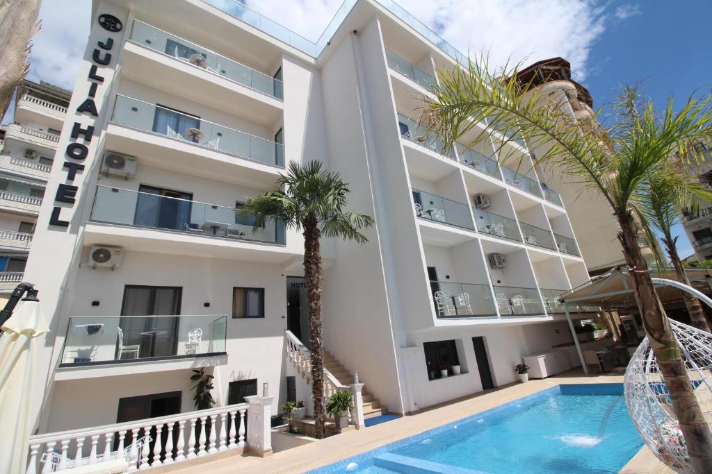 an apartment building with a swimming pool and palm trees at Julia Hotel in Sarandë