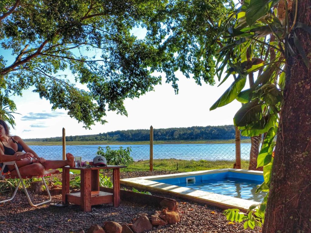 una mujer sentada en una silla junto a una piscina en La Casa Del Lago URUGUA-Í en Puerto Iguazú