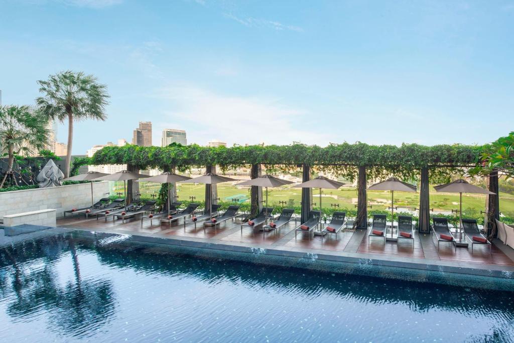 曼谷的住宿－曼谷瑞吉酒店，水边带椅子和遮阳伞的游泳池