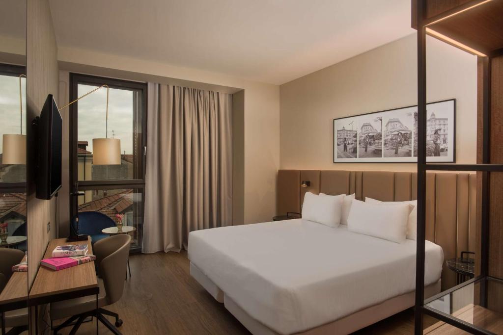 ミラノにあるNH Milano Corso Buenos Airesのベッドとデスクが備わるホテルルームです。