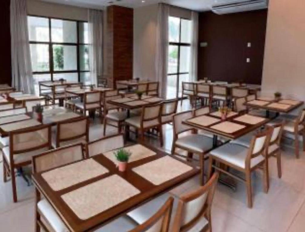 uma sala de jantar com mesas, cadeiras e janelas em Flat Hotel Samba Barra Jeunesse Arena Projac Rio Centro no Rio de Janeiro